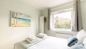 A bedroom with a bed, a window with curtains, a radiator, and a painting on the wall. - Quiet and Cosy 2-bed in Wimbledon (London)