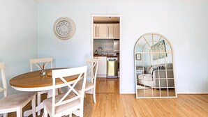A dining area with a wooden table and white chairs, a kitchen with beige cabinets, and a living area with a sofa and decorative mirror. - Quiet and Cosy 2-bed in Wimbledon (London)