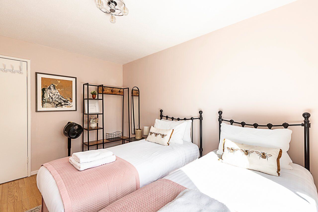 Une chambre avec deux lits, une table de chevet avec une lampe, une œuvre d’art encadrée et un miroir.