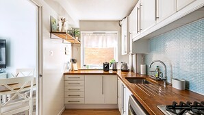 A modern kitchen with white cabinets, a wooden countertop, a gas stove, and a window with a view of a brick wall. - Quiet and Cosy 2-bed in Wimbledon (London)