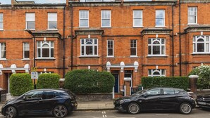 A row of red brick terraced houses with white-framed windows and a small front garden. - Stylish Hampstead Retreat by the Heath (London)