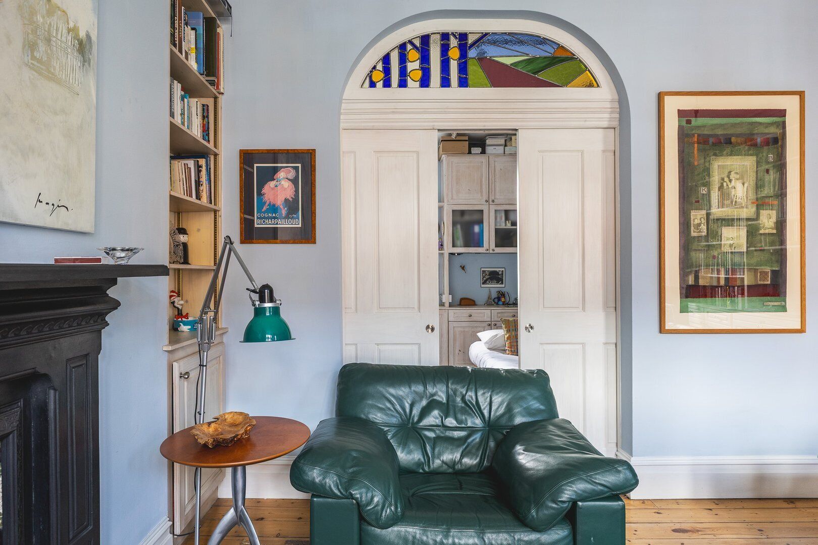 A cozy living room with a green leather sofa, a small wooden table, a bookshelf, and a fireplace.