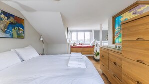 A bedroom with a large bed, a wooden dresser, and a window with a view. - Stylish Hampstead Retreat by the Heath (London)