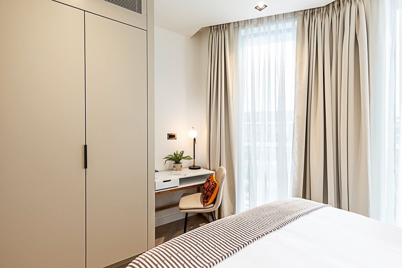 A hotel room with a bed, a desk, a chair, and a large window with curtains.