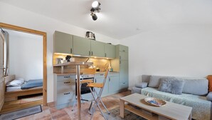 Un espacio habitable compacto con kitchenette, una mesa plegable, un sofá y una cama pequeña.
