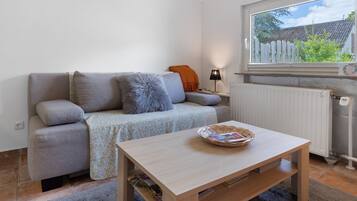 A living room with a sofa, a table, a lamp, and a window with a view of a house and trees.
