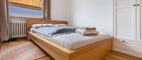 A single bed with a wooden frame, a window with curtains, a radiator, and a wardrobe.