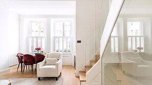 Ein modernes Wohnzimmer mit einem weißen Sofa, roten Sesseln, einem Esstisch mit Stühlen und einer Treppe mit Glastrennwand.