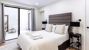 Ein modernes Schlafzimmer mit einem großen Bett, zwei Nachttischen mit Lampen, einer Schiebeglasdoor zum Balkon und Blick auf die Stadt.