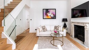 Ein modernes Wohnzimmer mit Treppe, einem weißen Sofa, einem Kamin und einem großen Fernseher.