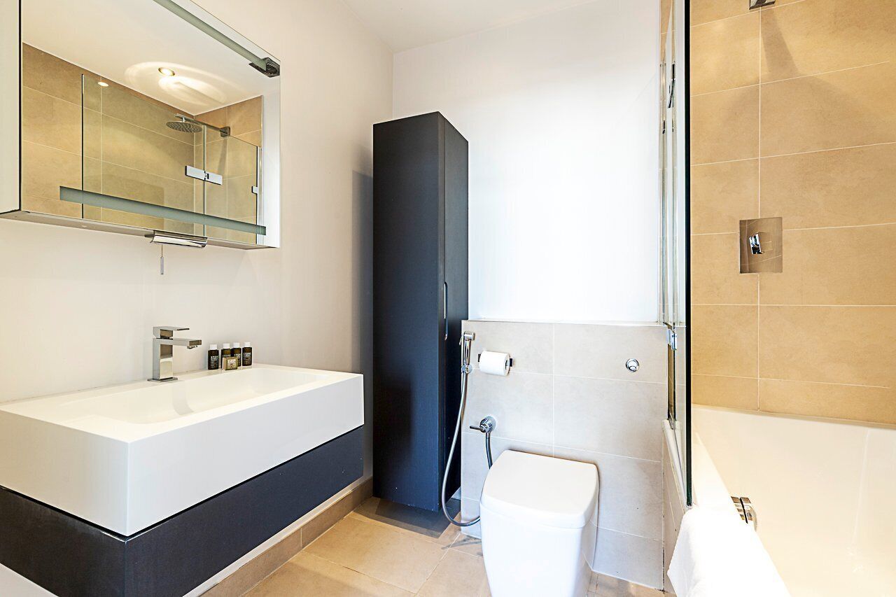 A modern bathroom with a large white sink, a dark cabinet, a glass shower enclosure, and a toilet.