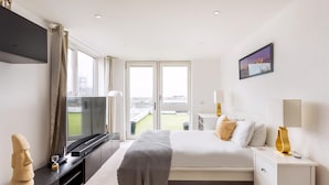 Ein modernes Hotelzimmer mit Bett, Nachttischen, einem Fernseher und einem großen Fenster mit Blick auf die Stadt.