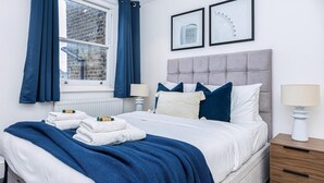 Een net opgemaakt bed met blauw-witte beddengoed, een bedlampje en een nachtkastje met een lamp.