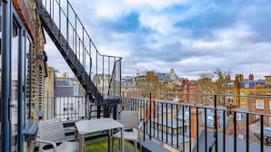Een balkon met een tafel en stoelen, een metalen hekwerk en uitzicht op de stad.