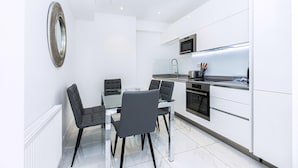 Een moderne keuken met witte kasten, een glazen eettafel en zwarte stoelen.