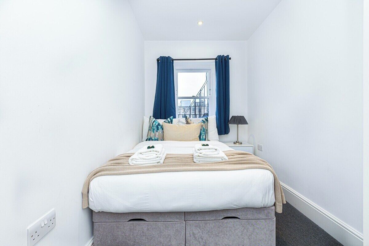 A hotel room with a bed, a window with curtains, a nightstand, and a lamp.
