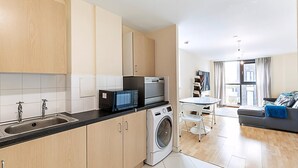 A modern kitchen with a washing machine, a microwave, and a sink. There is a dining area with a table and chairs.