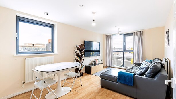 A modern living room with a dining table, sofa, and large windows offering a city view.