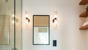 A modern bathroom with a glass shower enclosure, a white sink with a mirror above it, and two wall-mounted lights. - The Philbeach Three (London)