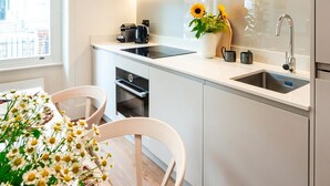A modern kitchen with white cabinets, a black countertop, a built-in oven, and a sink with a faucet. There is a window with a view of buildings outside. - The Philbeach Three (London)