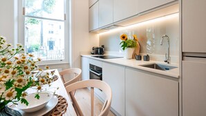 A modern kitchen with white cabinets, a stainless steel sink, and a window with a view of buildings outside. - The Philbeach Three (London)