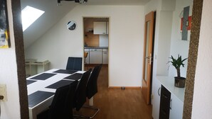 A dining area with a table and chairs, a kitchen in the background, and a ceiling light fixture. - Apartment 'Eckert' with Shared Garden, Balcony and Wi-Fi (Wehr)