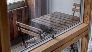 Un banco de madera con estructura metálica y un cojín, ubicado cerca de una ventana de madera.