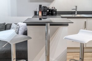 A modern kitchen with a central island, two bar stools, a coffee machine, and a sink. - Canning Town Pied-à-terre (London)