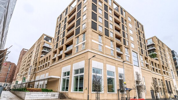 Un edificio de varios pisos con un diseño arquitectónico moderno, que presenta una entrada destacada en esquina, ventanas amplias y balcones.