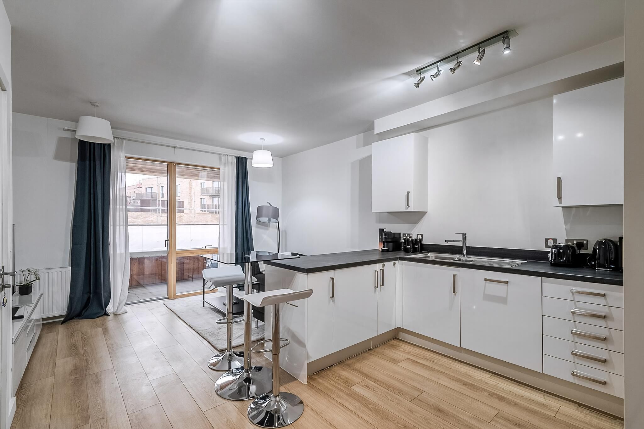 A modern kitchen with white cabinets, a black countertop, and stainless steel bar stools.
