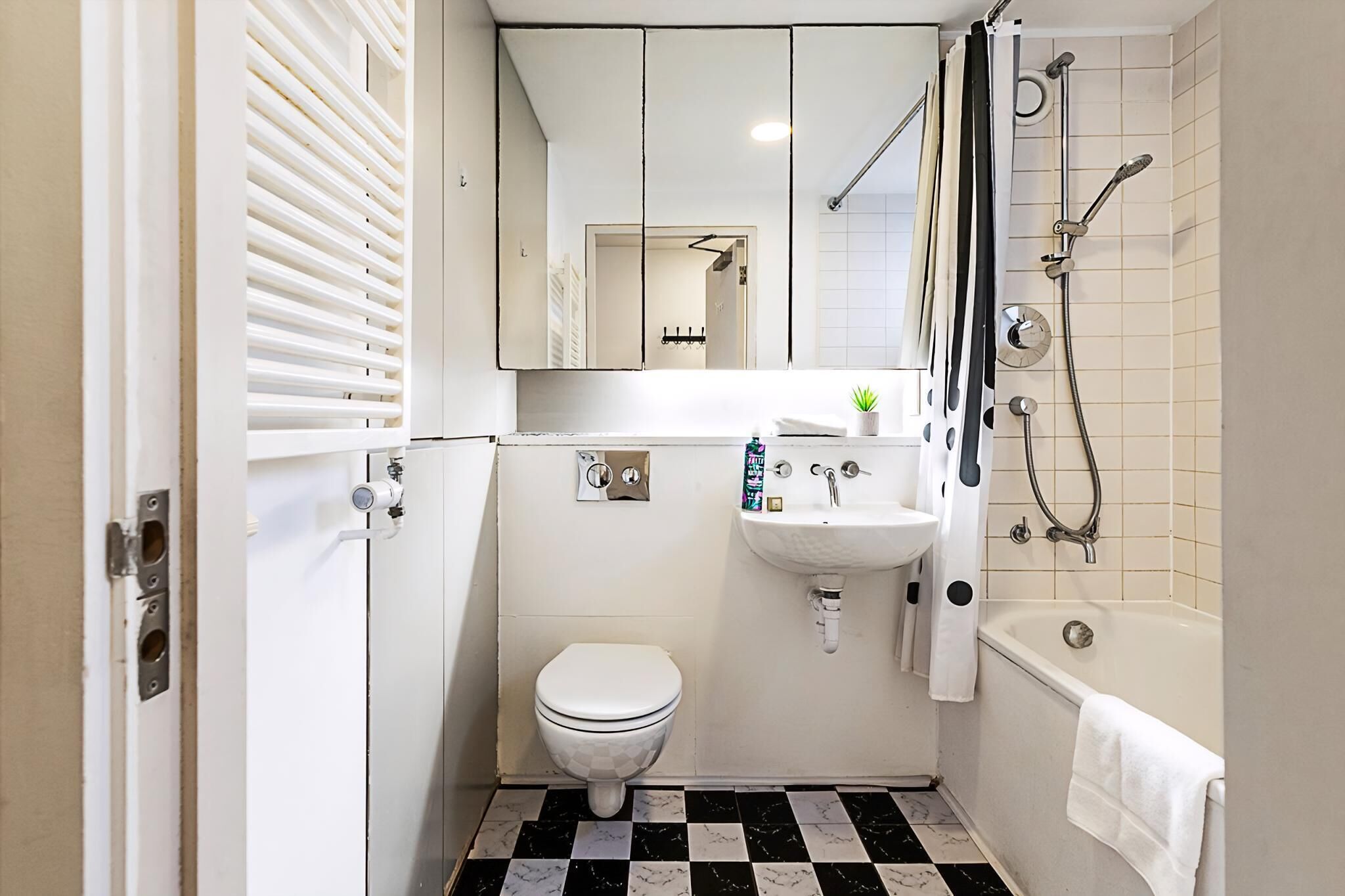 Une petite salle de bain comprenant des toilettes, un lavabo et une baignoire, avec un carrelage à motifs et des éléments d’équipement blancs.
