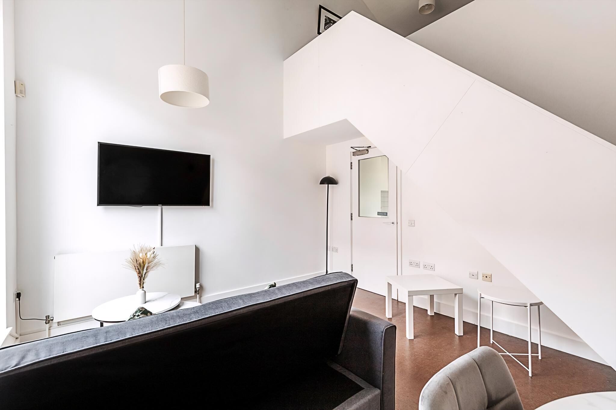Et moderne værelse med et fladskærms-tv, et skrivebord, en stol, en sofa og en trappe.