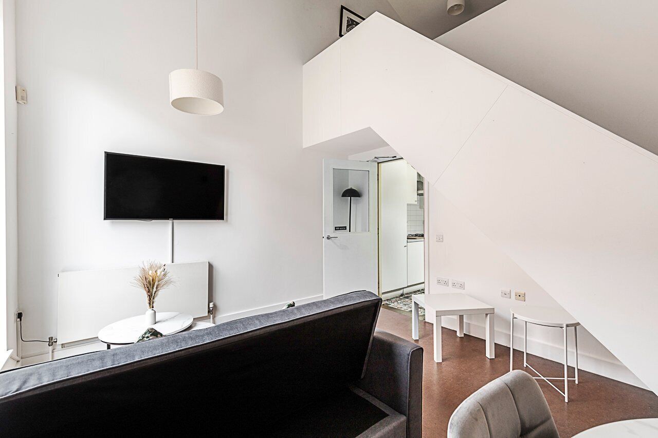 A modern interior with a black sofa, a flat-screen TV, a white table, and a staircase.