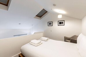 A modern hotel room with a bed, a chair, a skylight, and two framed pictures on the wall.
