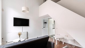 En modern inredning med en platt-TV, en vit soffa, ett matbord och en trappa.