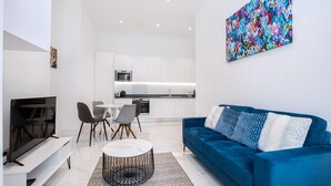 Una sala de estar moderna con un sofá azul, un televisor y un comedor con sillas y una mesa.