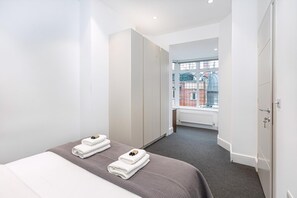 Quarto de hotel com cama, duas toalhas, janela e vista para um edifício.