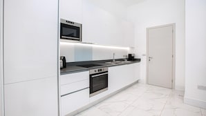 Una cocina moderna con armarios blancos, horno empotrado, microondas y cafetera.