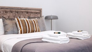 Una cama bien hecha con un cabecero capitonado, almohadas a rayas y toallas dobladas.