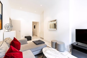 A modern living room with a sofa, ottoman, TV, and a fan.