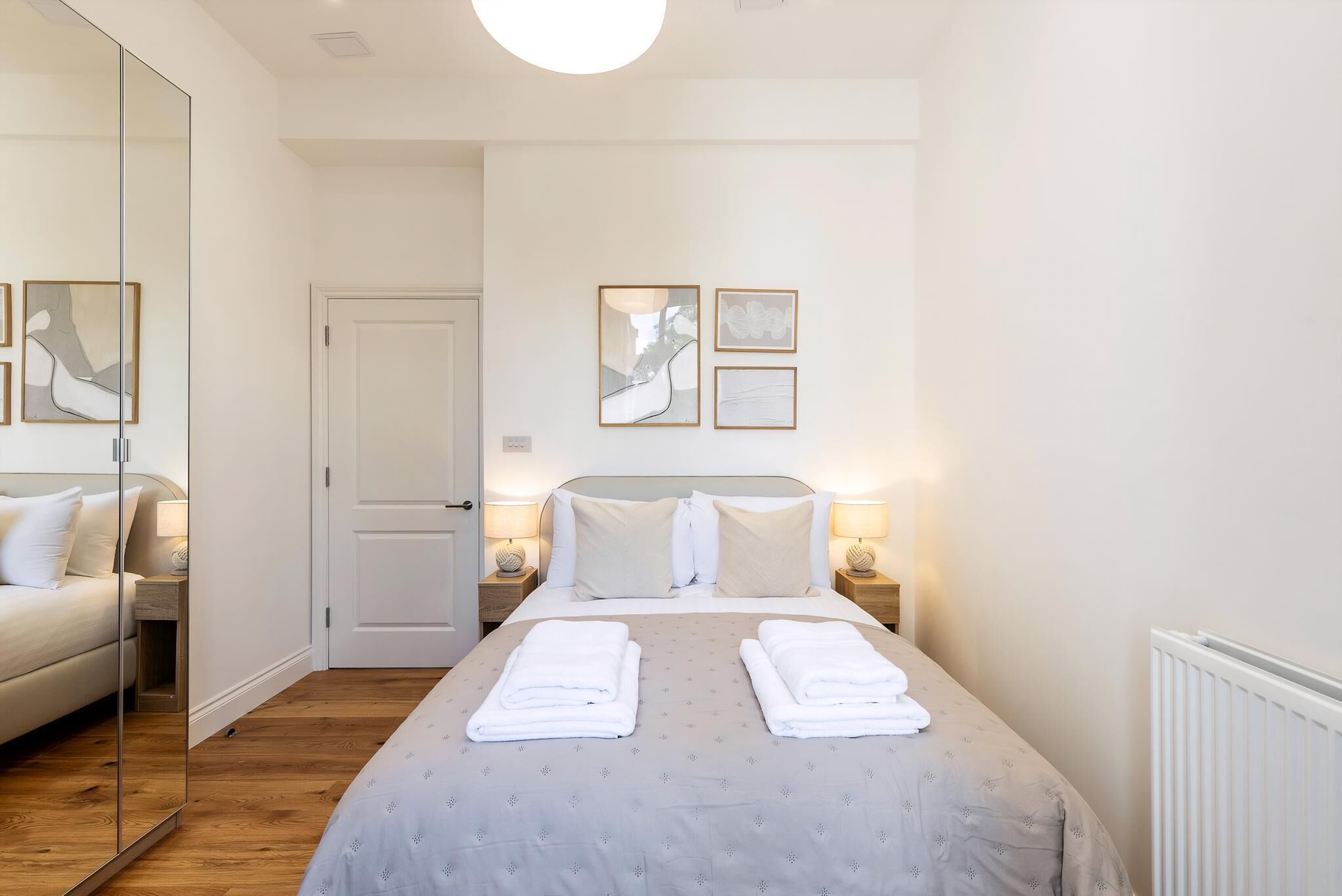 Habitación de hotel con una cama grande, dos mesitas de noche con lámparas, un espejo y cuadros en la pared.