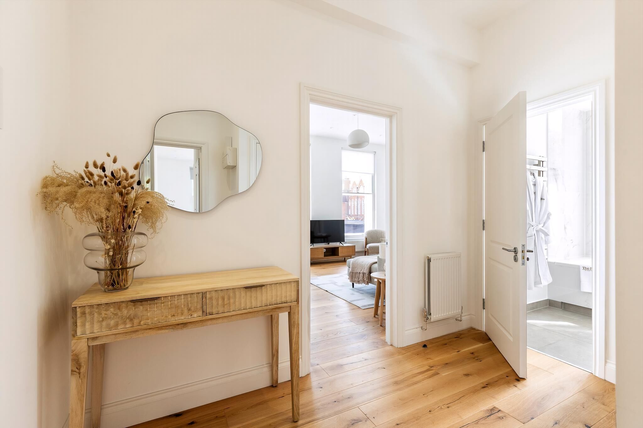 A hallway with a wooden console table, a mirror, and a door leading to a bathroom.