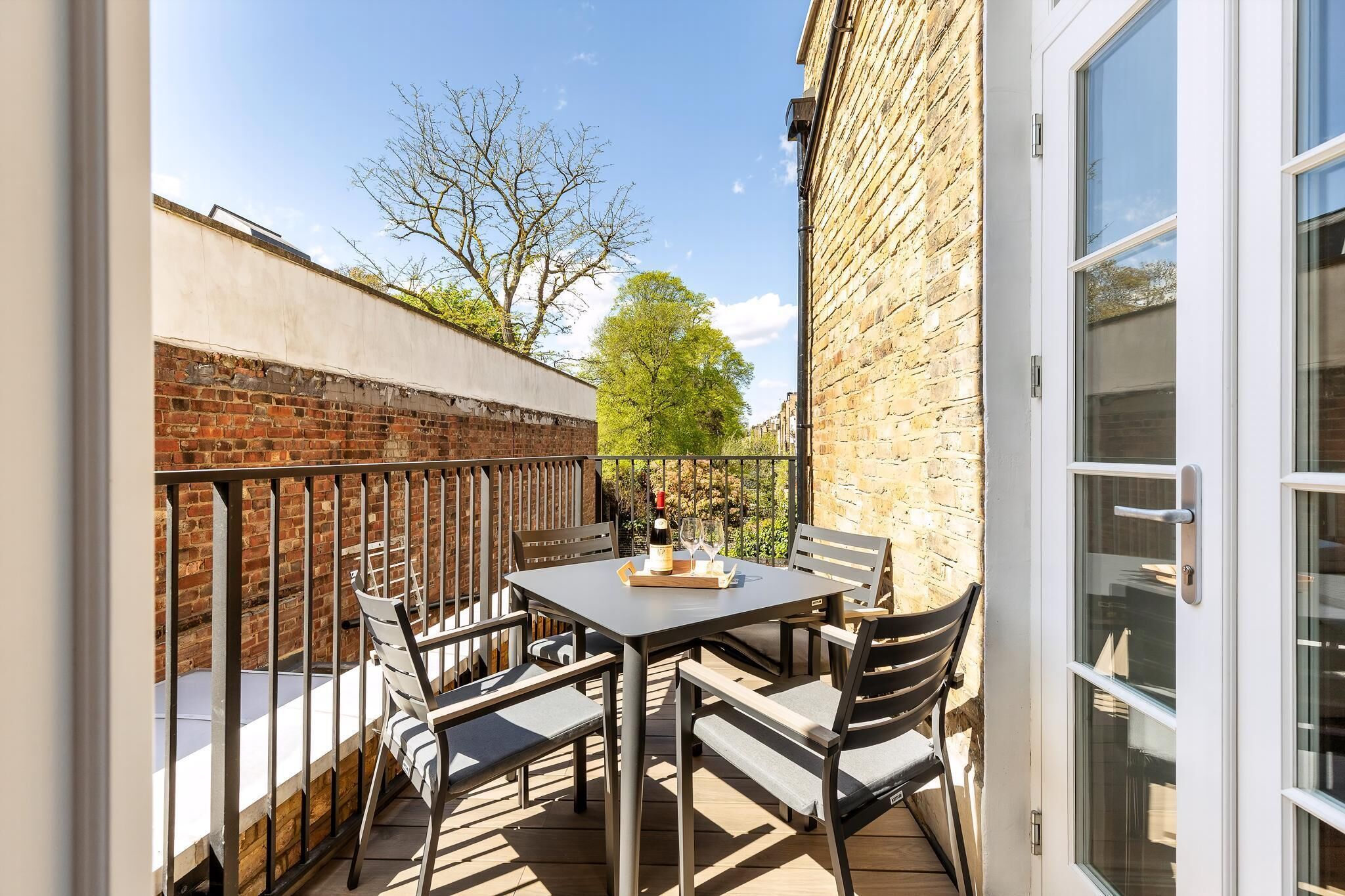 A patio with a table and chairs, a bottle of wine, and a glass on the table.
