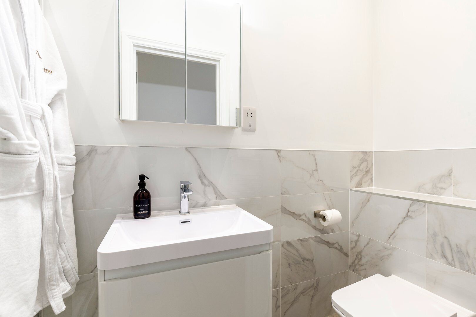 A bathroom with a white sink, a mirror above it, and a marble-tiled wall.