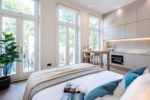A modern bedroom with a bed, bedside table, and a view of a balcony with a potted plant. - The Philbeach Five (London)