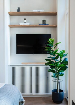 Una sala de estar moderna con un televisor de pantalla plana, estanterías de madera, un radiador y una planta en maceta.