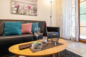 Una sala de estar con un sofá de cuero, una mesa de centro con una botella de vino y una copa, y una obra de arte floral en la pared.