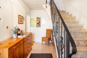 A staircase with a black handrail, a wooden bench, a wicker chair, and a bulletin board with various papers and a map.