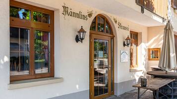 A building with a sign reading 'Hannlins' and 'Straußi' on the facade, a wooden door, and a table with an umbrella outside.