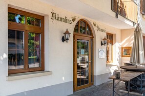 A building with a sign reading 'Hannlins' and 'Straußi' on the facade, a wooden door, and a table with an umbrella outside.